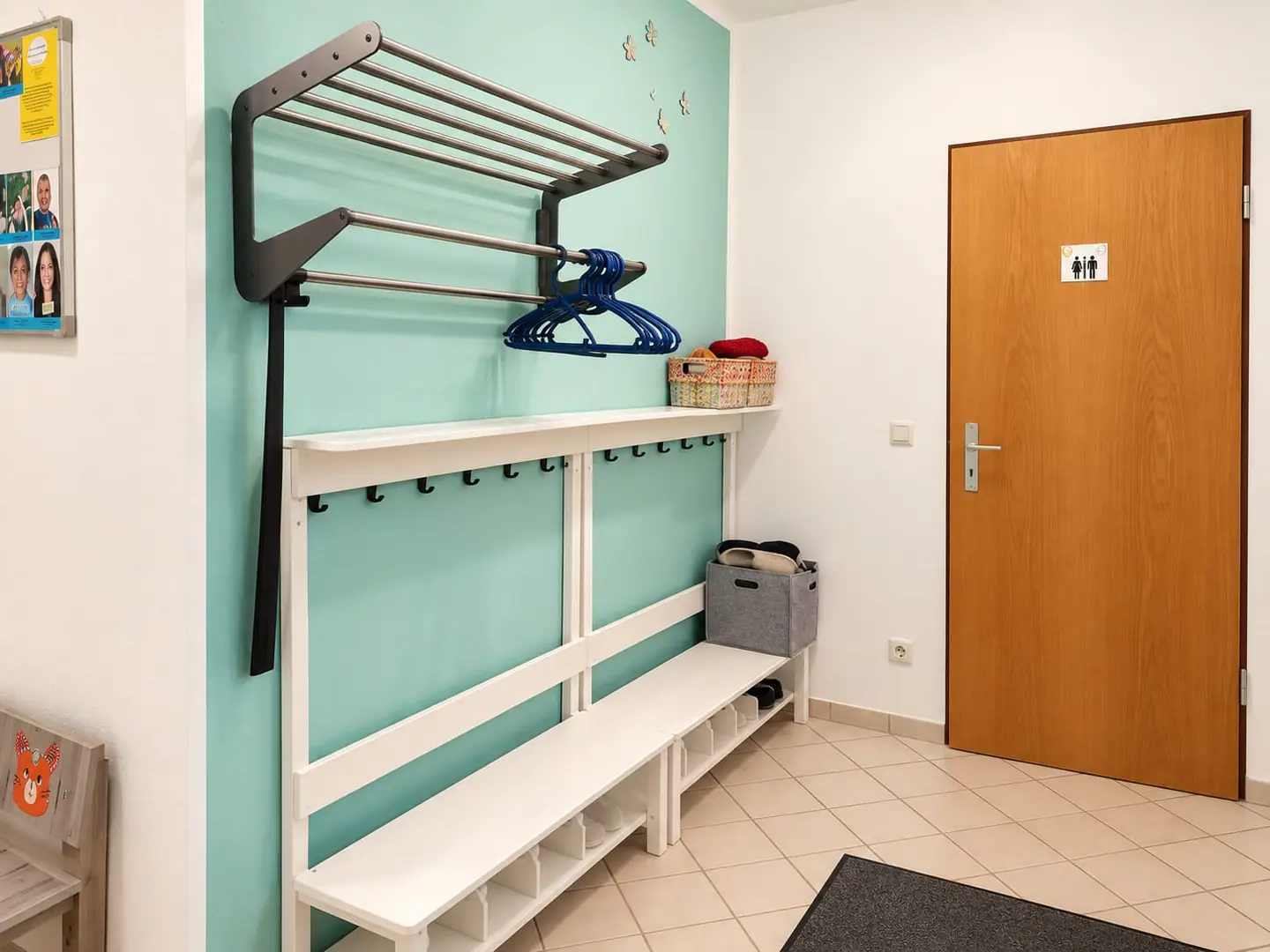 Garderobe mit mintgrüner Wand, Kleiderhaken, Schuhbank und Körbchen.