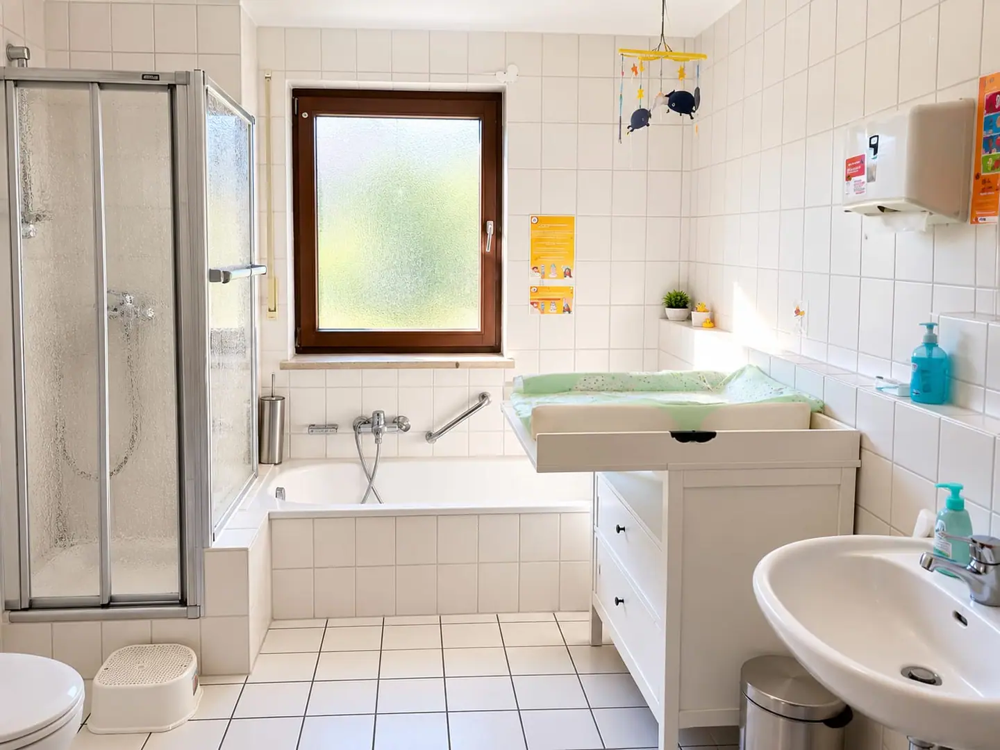 Helles Bad mit Wickelkommode, Babybadewanne, Dusche und Kinder-Toilettenhocker.